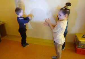 Troje dzieci tworzy cienie ze swoich dłoni na ścianie.